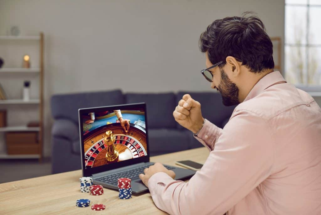 A man seated at a table, focused on a laptop while playing roulette in an online casino